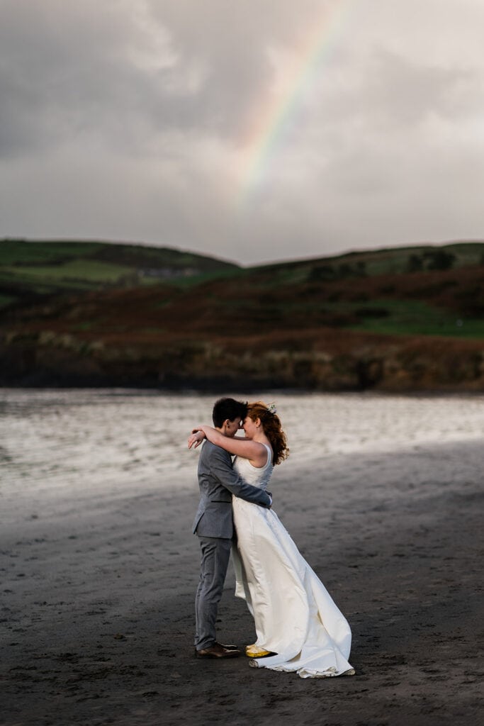 couple kiss on beach with rainbow in background