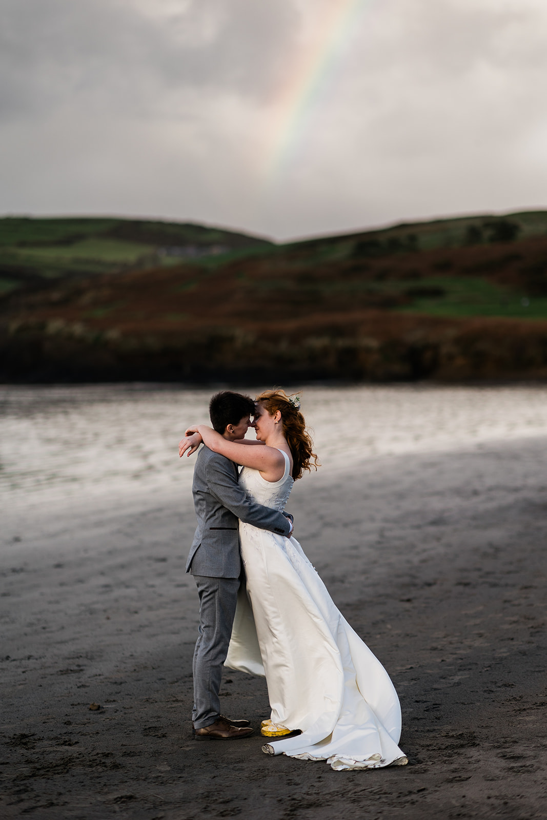 bride and bride kissing on a beach under a rainbow