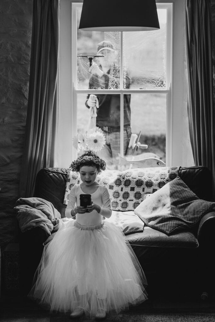 little girl looks at a phone while a window cleaner cleans the window behind her. swansea wedding photographer John Wellings